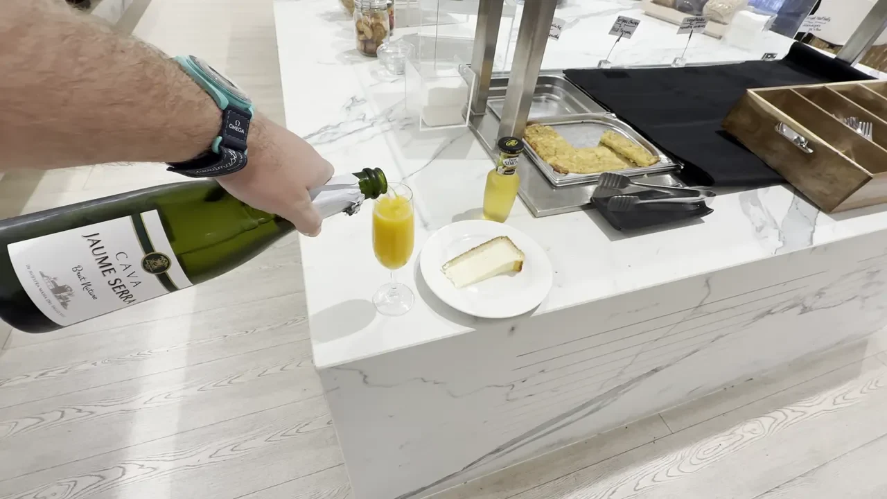 Bottle of cava being poured into a glass with a slice of cake and buffet hot trays on the counter at Tenerife South lounge